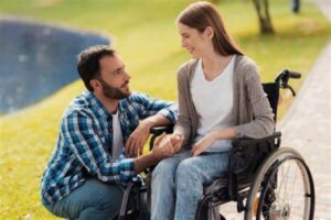 Photo d'une femme et fauteuil roulant et d'un homme acroupie à son niveau.