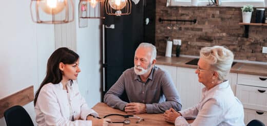 Photo de deux personnes âgées et un professionnel assisent autour d'une table dans la cuisine.
