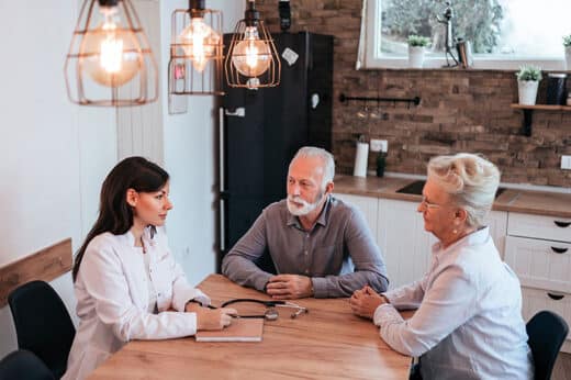 Photo de deux personnes âgées et un professionnel assisent autour d'une table dans la cuisine.