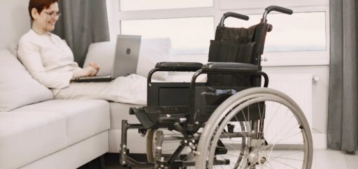 Photo d'un fauteuil roulant électrique au première plan et d'une femme assise en arrière plan sur un canapé.
